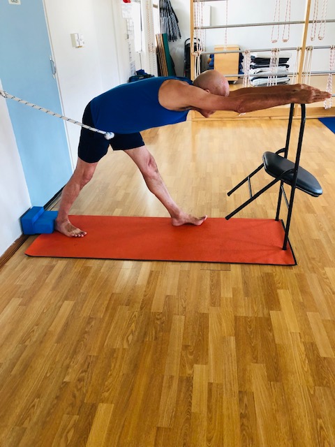 A man stretching at the rope wall with his hands on a chair, a supported pose for back, neck and shoulders