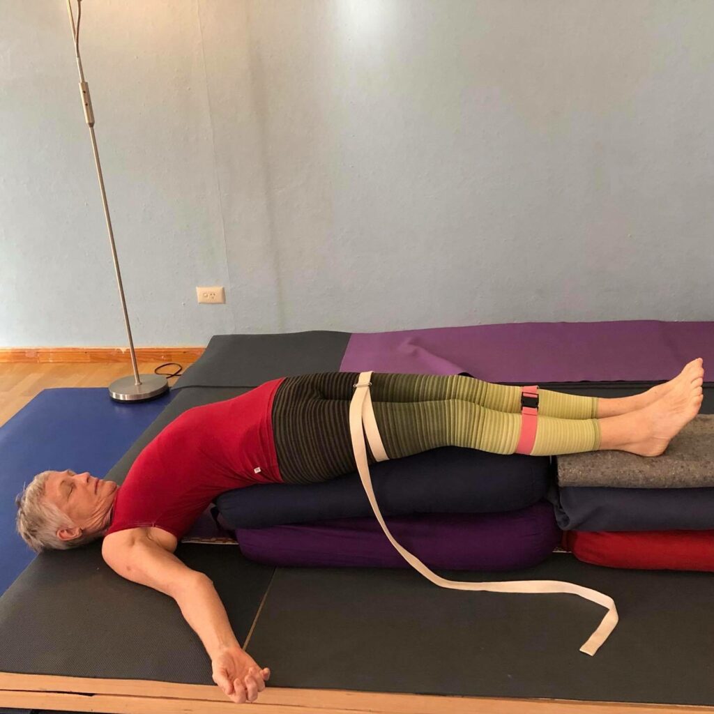 Chris lying back over stacked bolsters with a strap