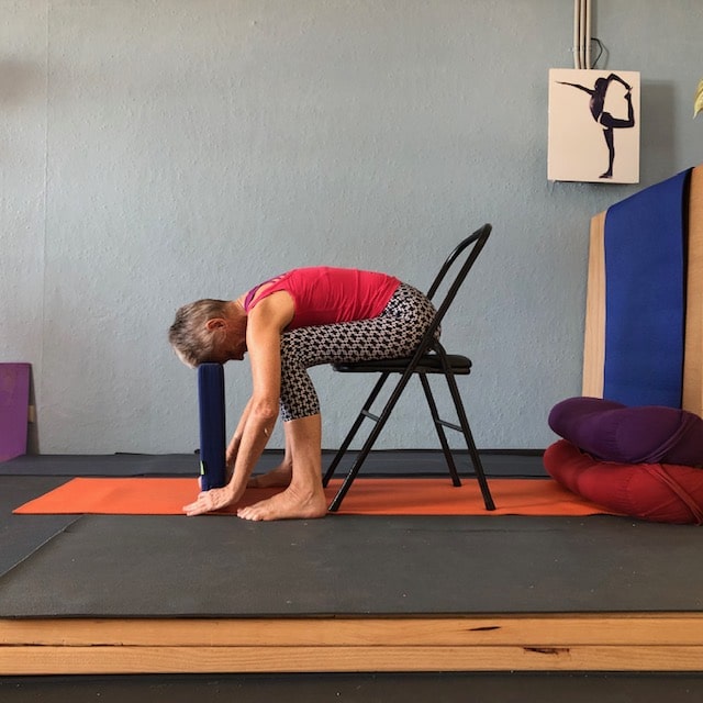 Standing forward bend with the forehead resting on blocks and hands on a chair, letting the neck release