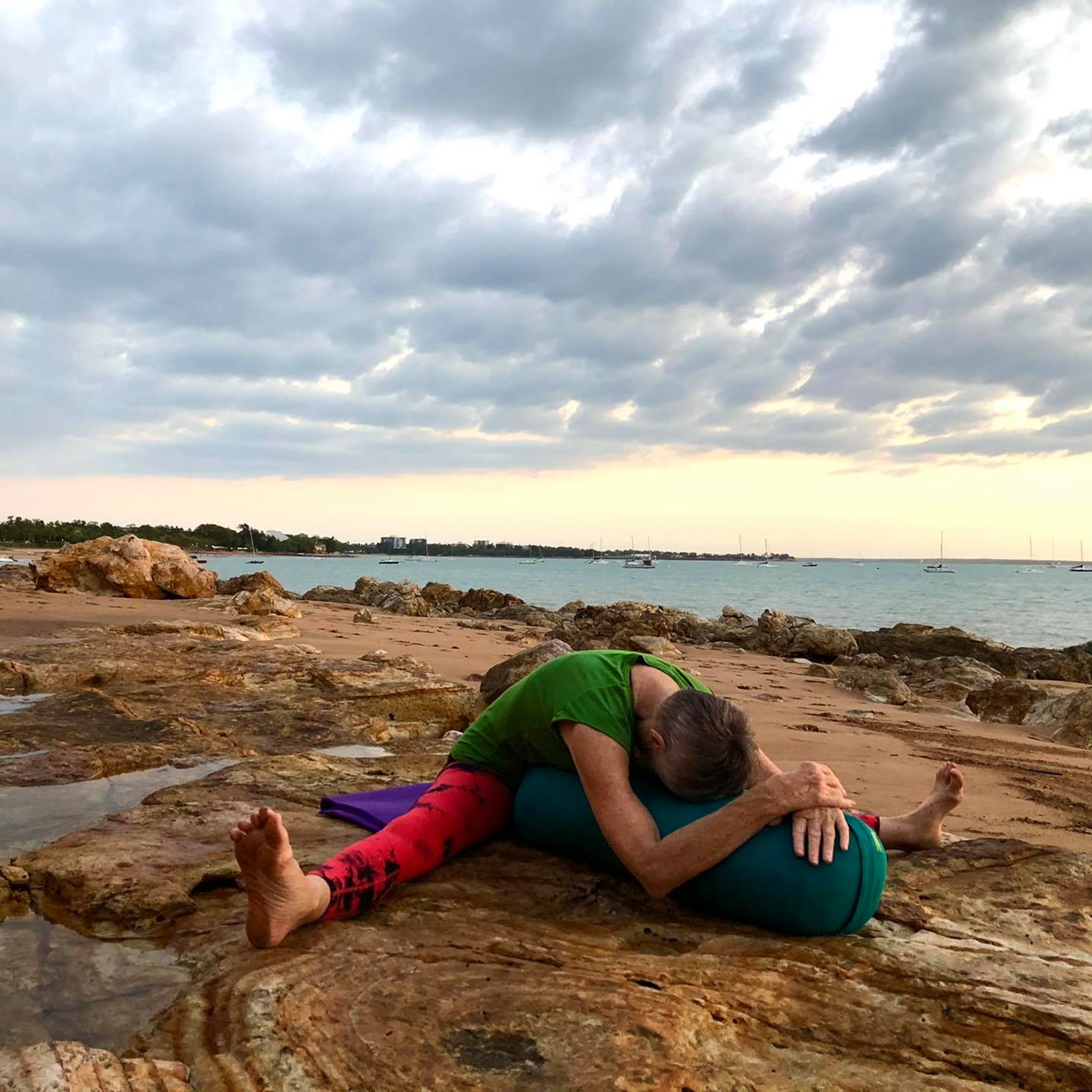 Benefits of forward bends: a supported forward bend over a bolster on the rocks