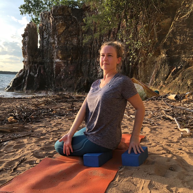 Yoga poses for anger: a seated twist on the beach with the hands on blocks and the chest turning