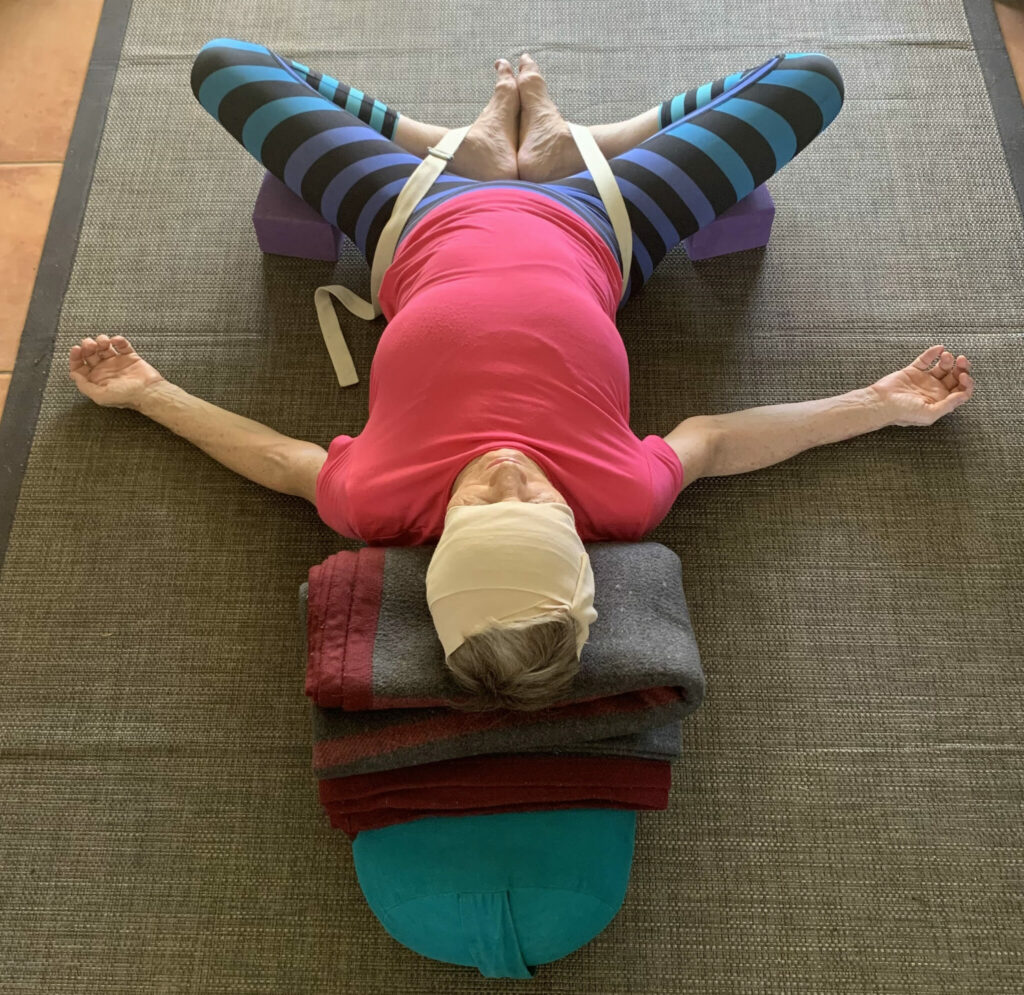 Restorative yoga for anxiety: Reclining Bound Angle Pose over a bolster, the head wrapped and the knees supported on blocks
