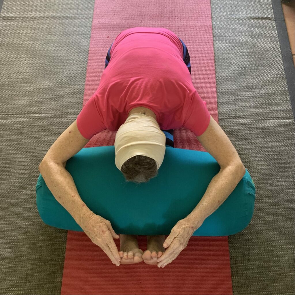 Vagus nerve yoga: a supported forward bend with the forehead resting on a bolster and the head wrapped