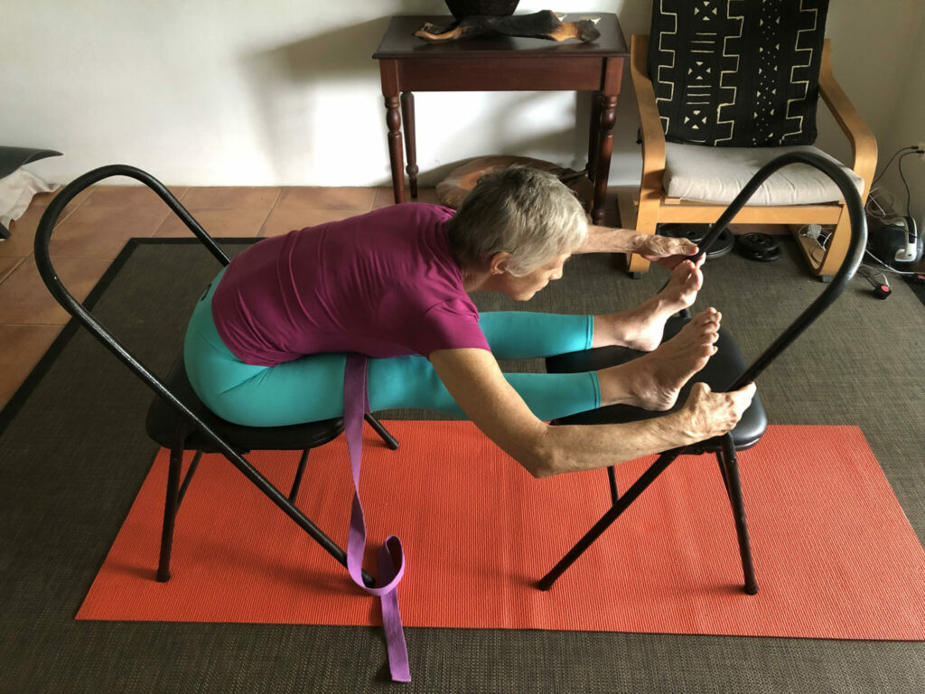 Chris folding forward over a chair with a strap