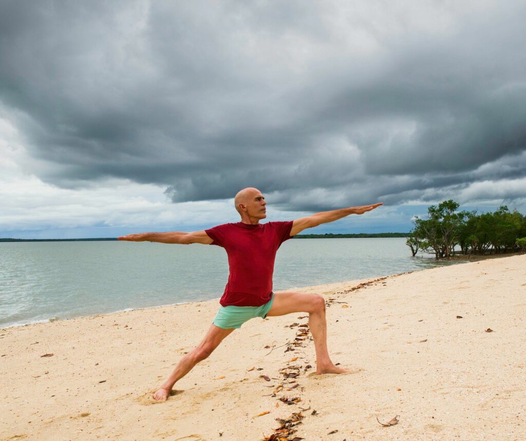 Stuart McGill in Warrior 2 on a Top End beach, front knee bent over the ankle, back leg straight, arms reaching out