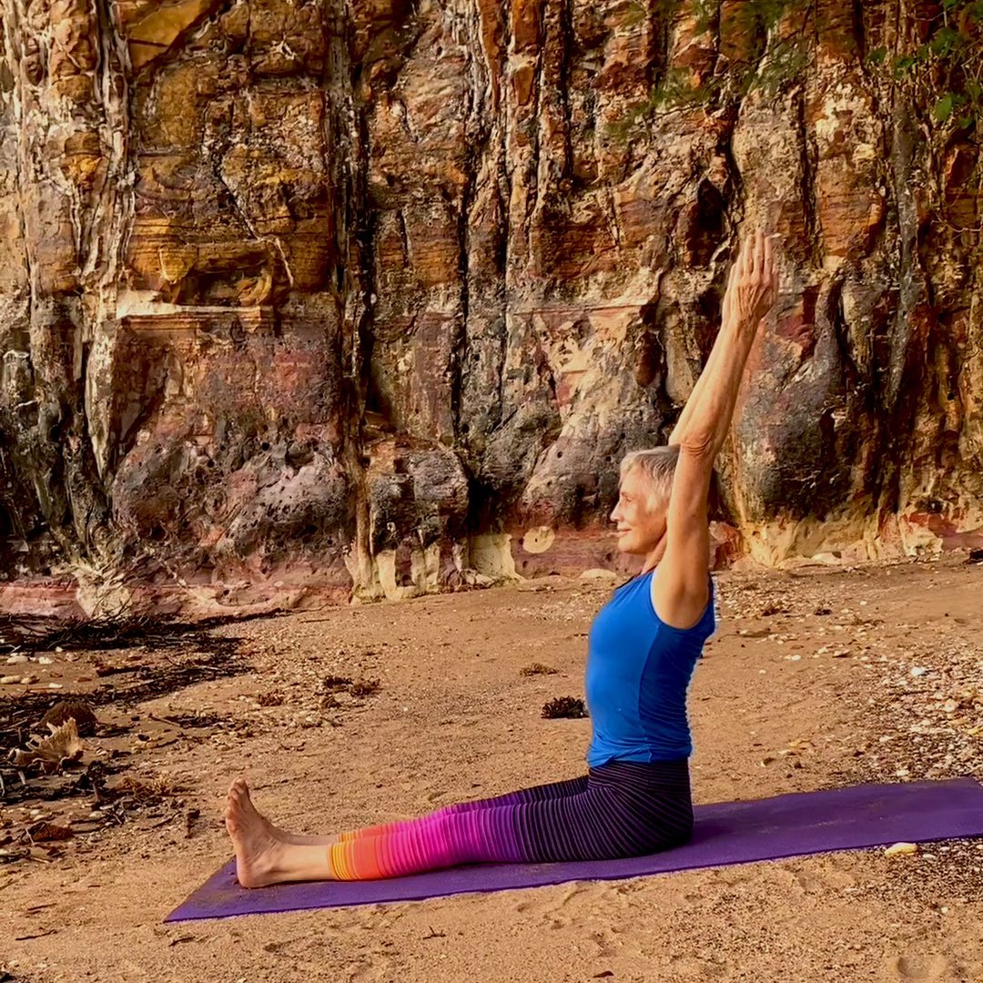 Chris Lalor sitting upright on the floor with her arms raised, keeping the natural curve of the lower back