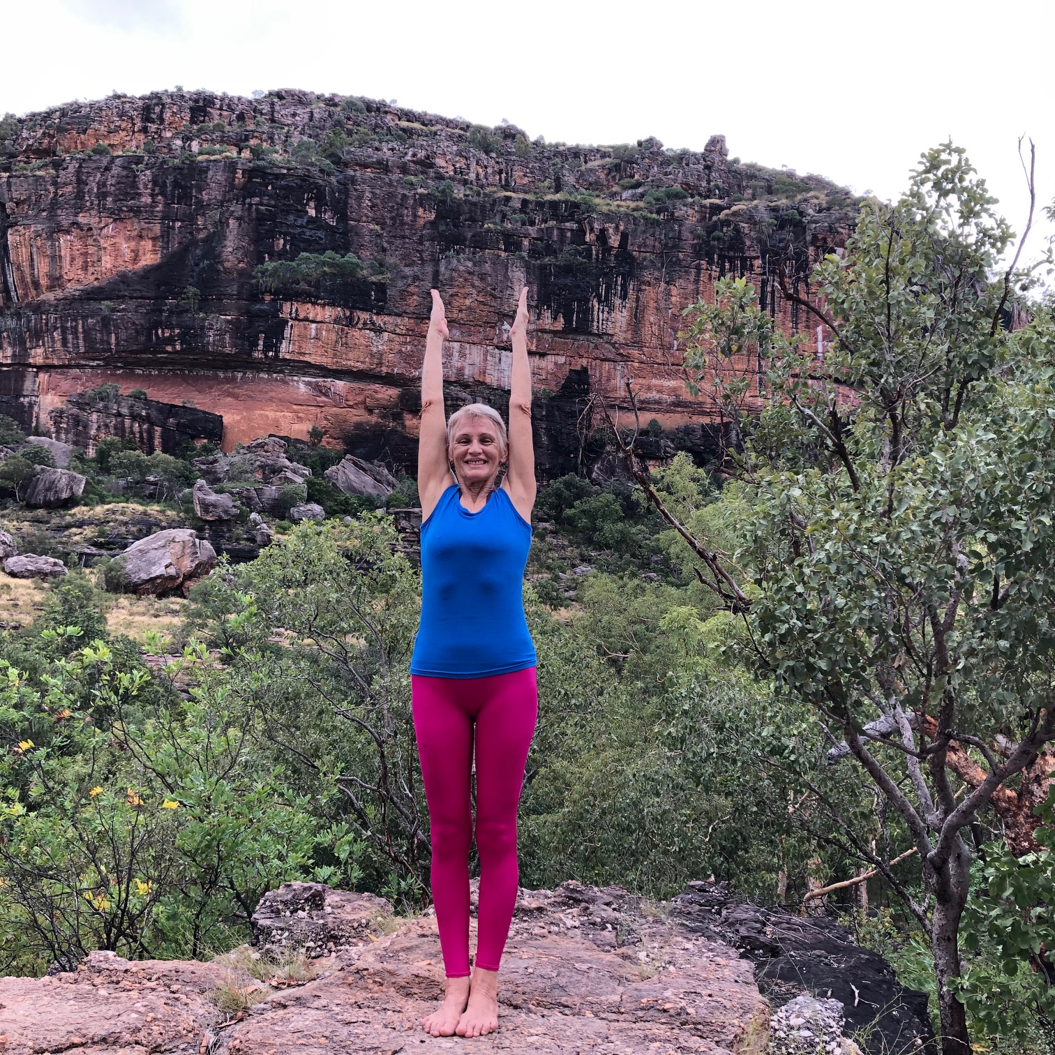 Iyengar yoga: Chris Lalor in Upward Hands Pose, arms straight beside the ears, in front of a sandstone escarpment
