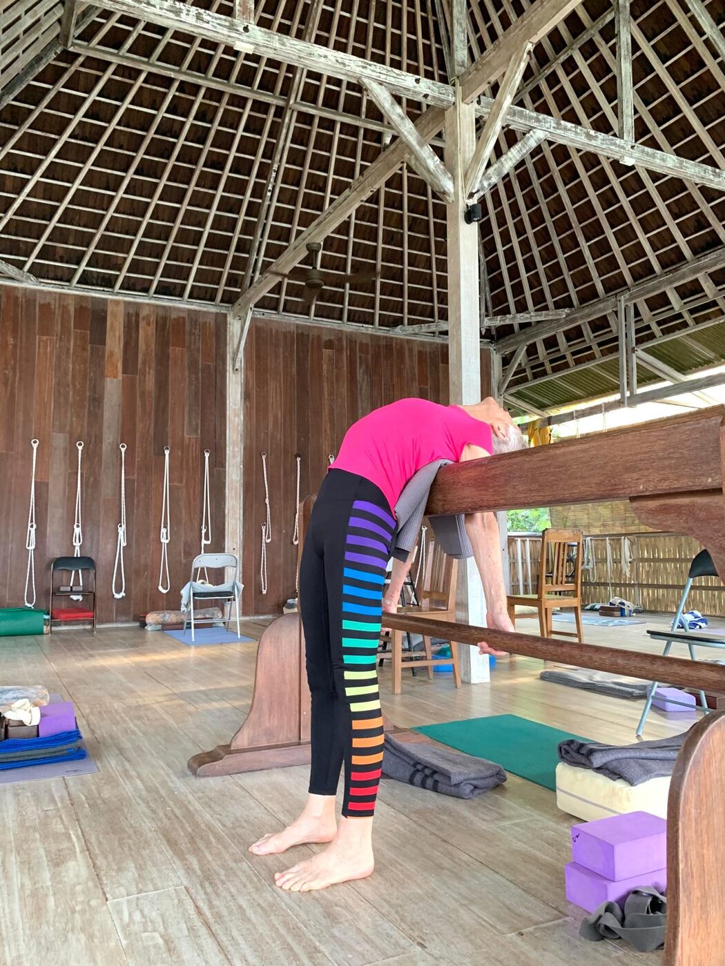A supported forward bend over the wooden bar in the yoga room at Pondok Pisang