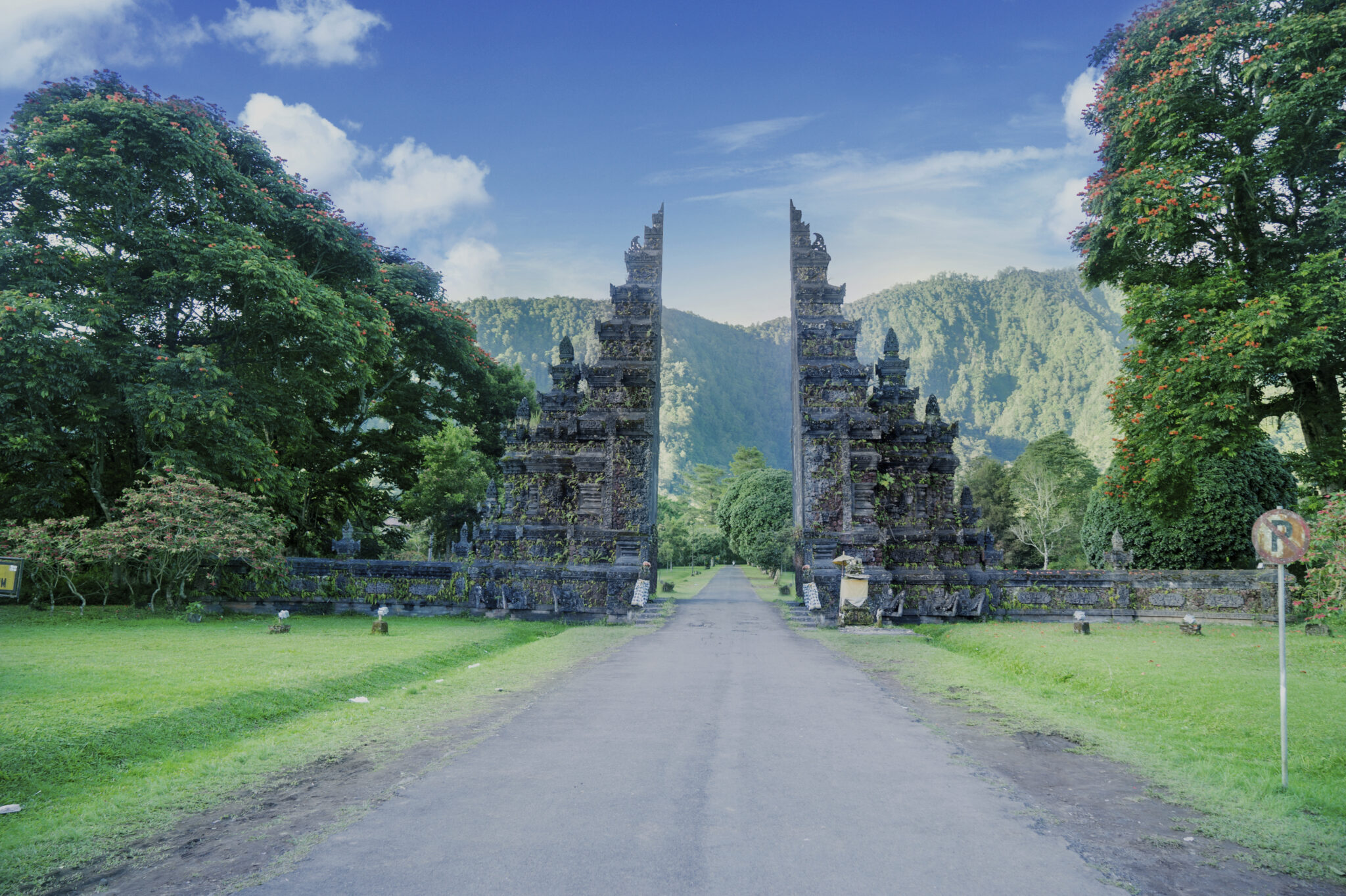 The carved stone Handara gate standing across the road at Bedugul in the Bali highlands, with forested hills behind