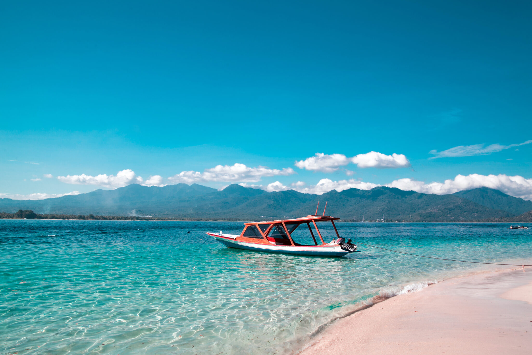 A wooden boat moored in shallow turquoise water off the white sand of Gili Trawangan, with the hills of Lombok behind