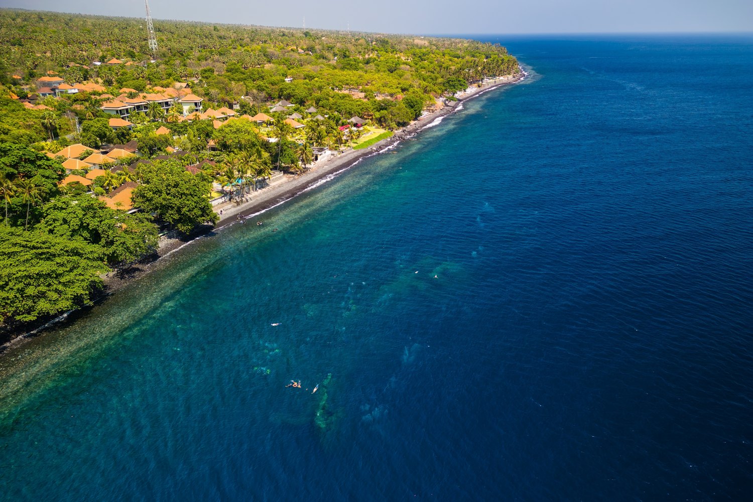 Aerial view of the black sand beach and village at Tulamben in east Bali, with snorkellers and divers in the clear water over the wreck