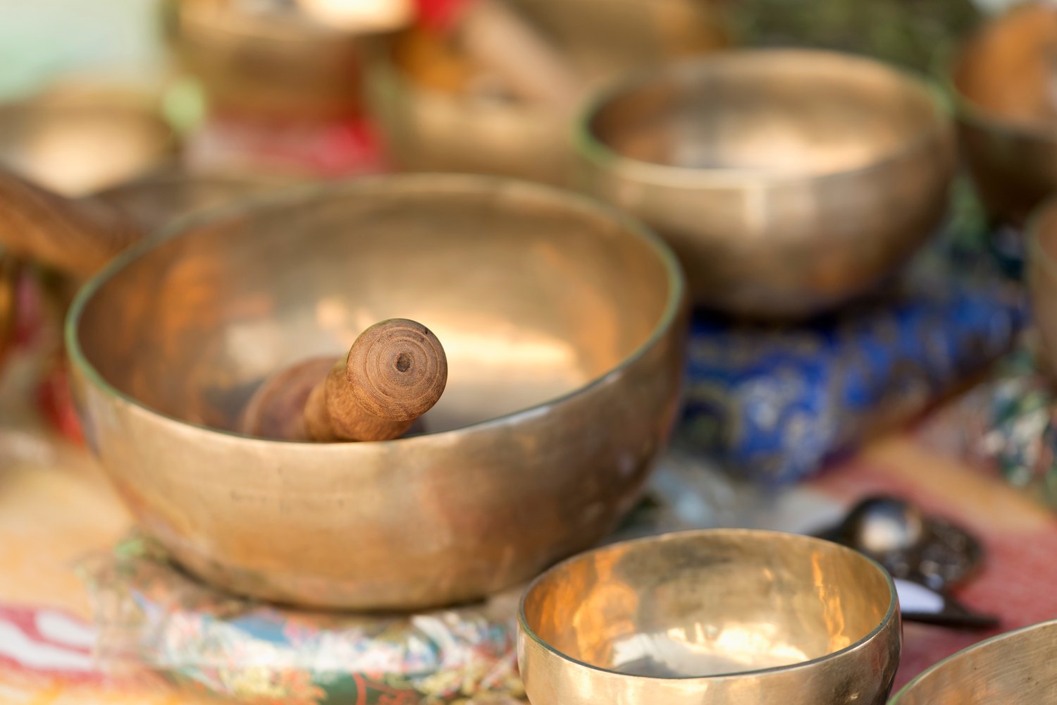 Several hand beaten brass Tibetan singing bowls of different sizes laid out on cloth, with a wooden mallet resting in the largest