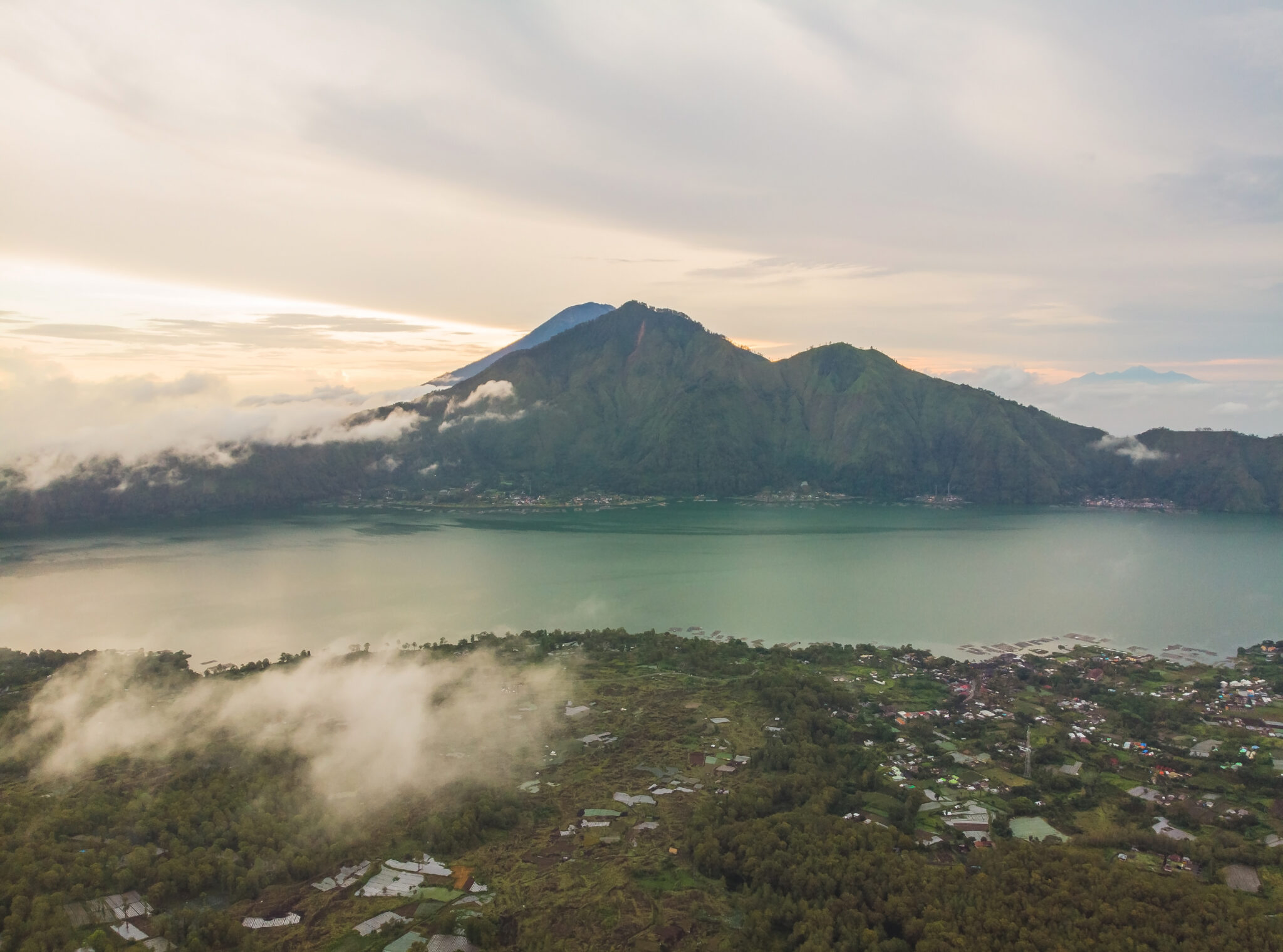 Mount Batur and the caldera lake seen at sunrise from the Kintamani rim, with cloud lying in the valley below