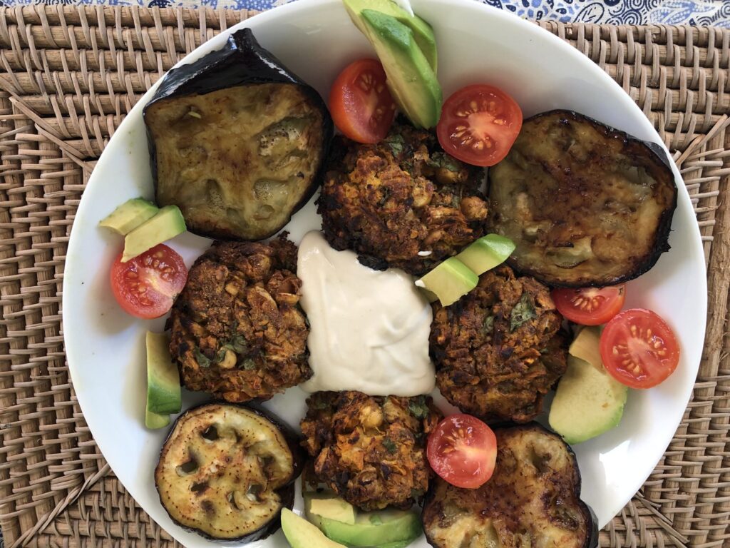 Baked chickpea patties with eggplant, cherry tomatoes, avocado and tahini on a white plate