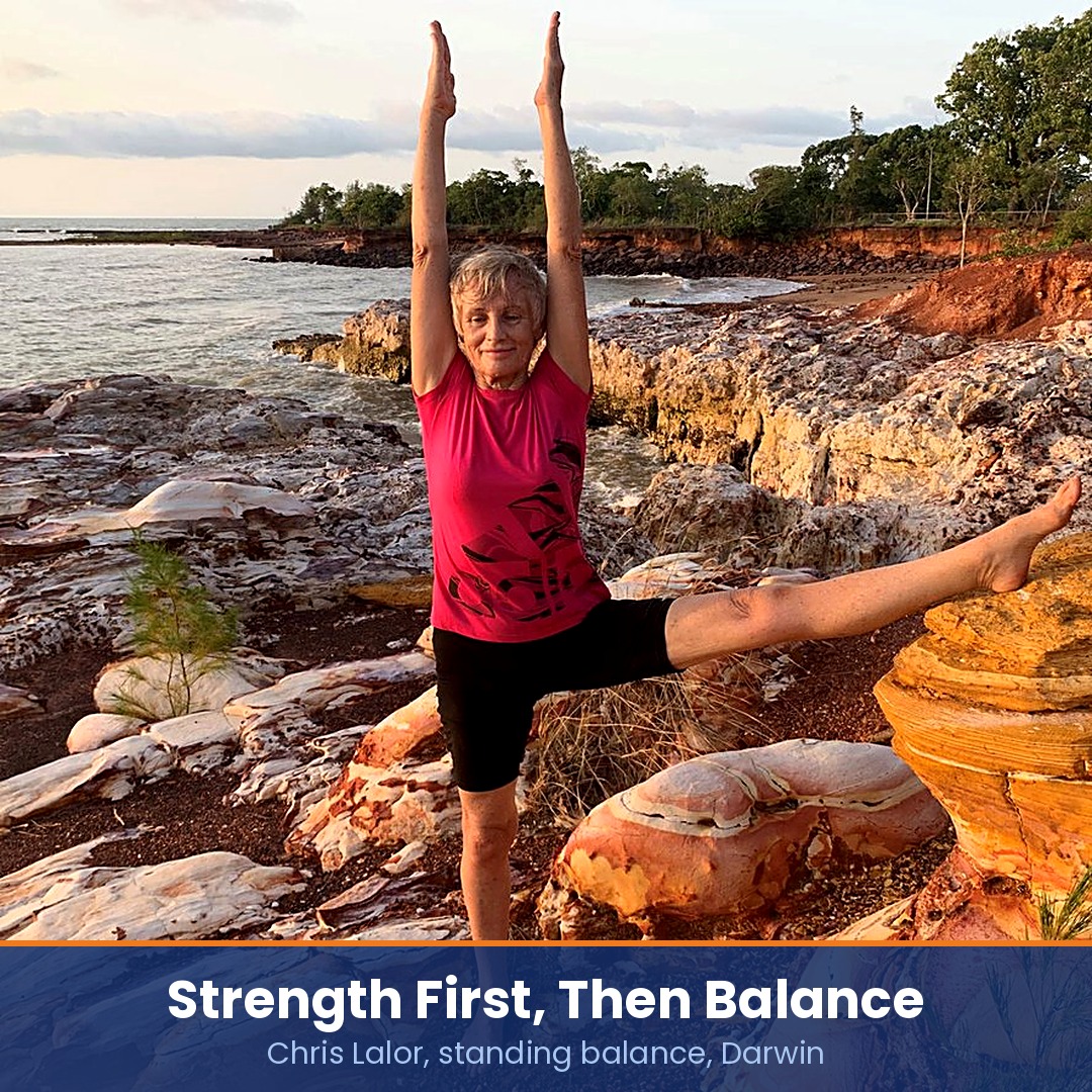 Yoga for balance: Chris Lalor in a standing balance pose on red rock by the sea near Darwin, arms overhead and one leg extended