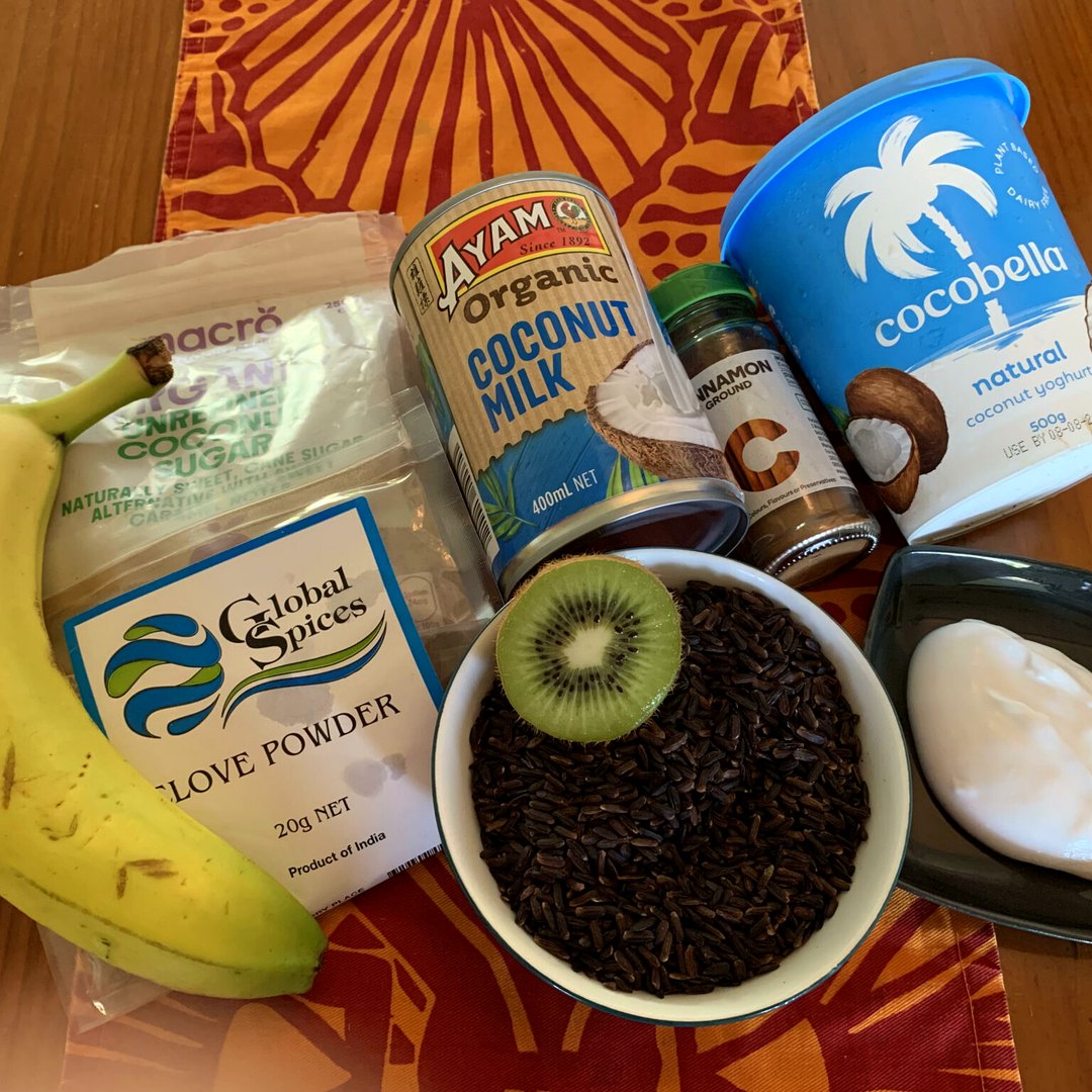 Yoga retreat experience: ingredients for black rice pudding laid out on a table, with a bowl of black rice topped with a slice of kiwi fruit, coconut milk, coconut yoghurt, spices and a banana