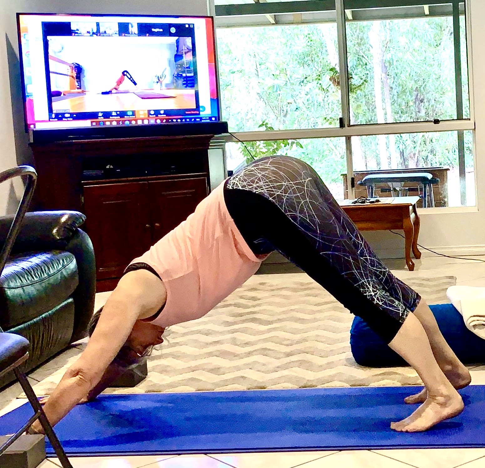 Student at home in a live online yoga class, camera on, teacher on the screen