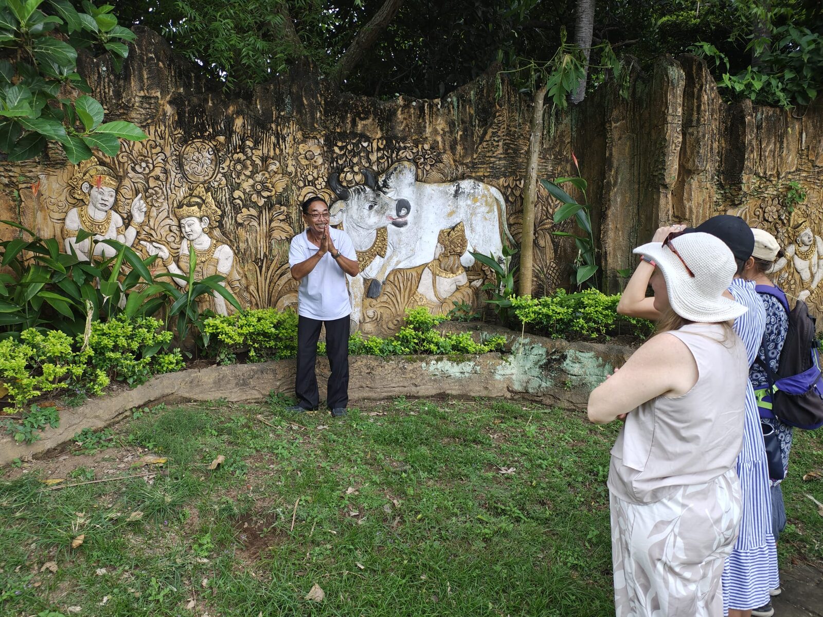 A local guide explaining the carved relief wall to Flametree retreat guests at Taman Ujung, Bali