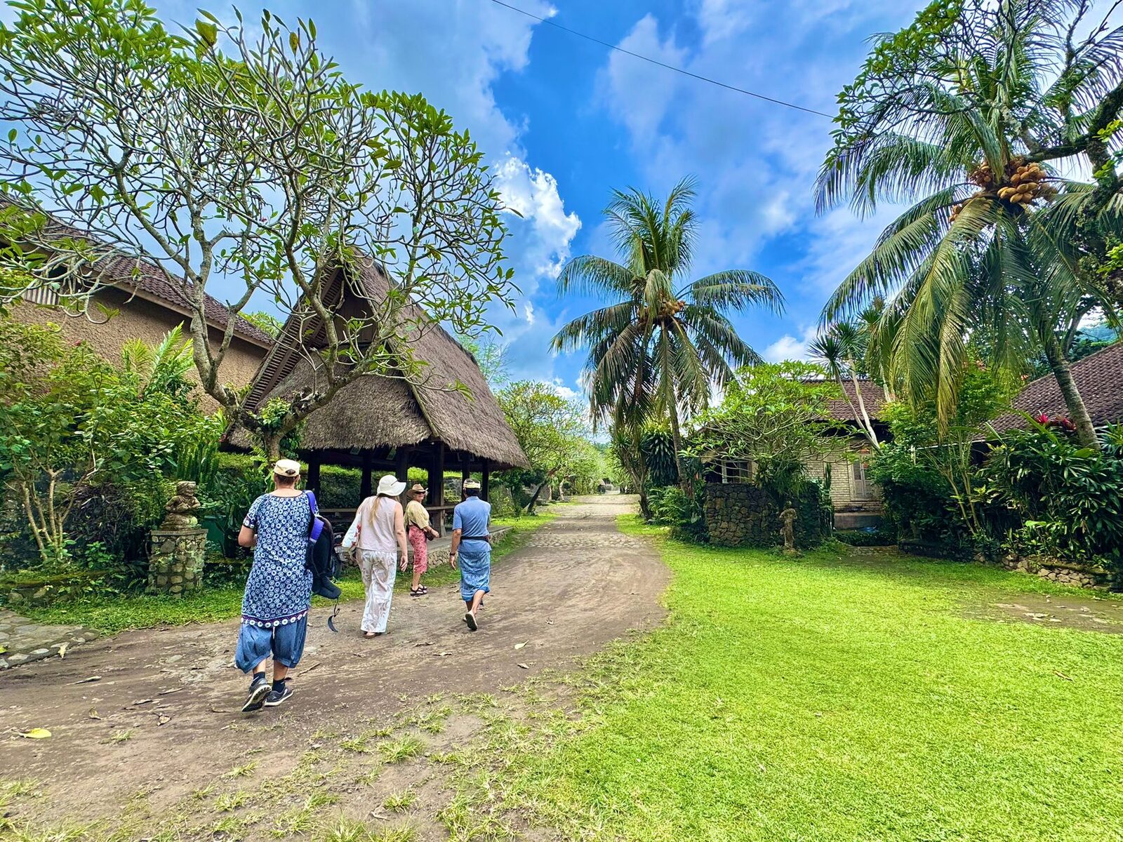 The wide grass avenue between the pavilions in Tenganan village with Flametree retreat guests walking
