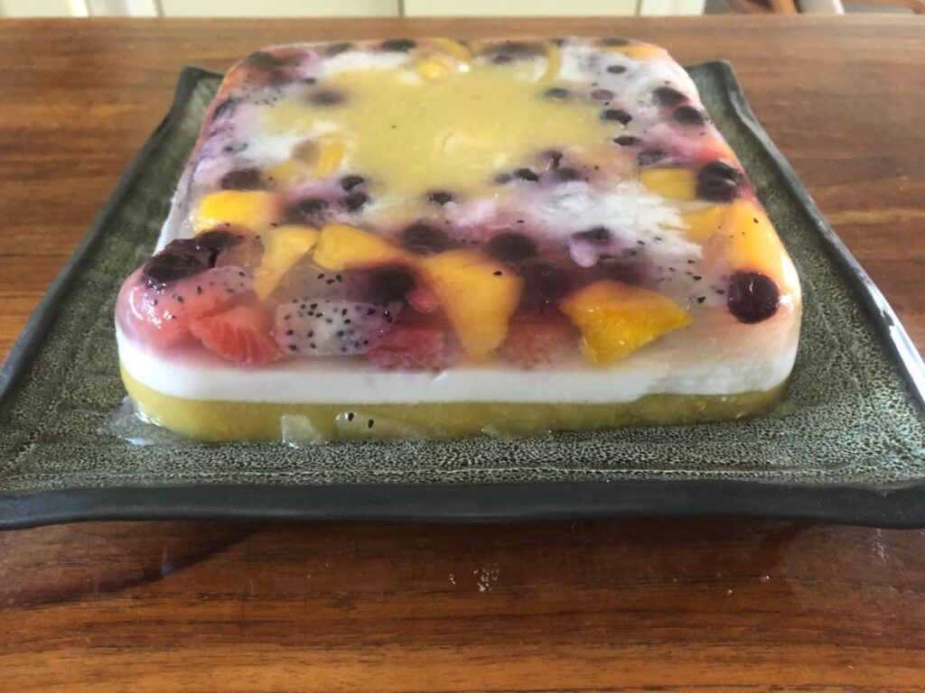 Layered agar agar dessert with jackfruit, coconut milk, mango and blueberries on a green plate