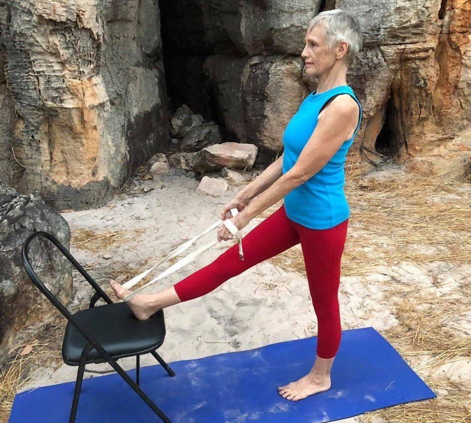 Bone density Darwin: a woman in a supported standing lunge with a chair, front knee bent, back leg long and strong