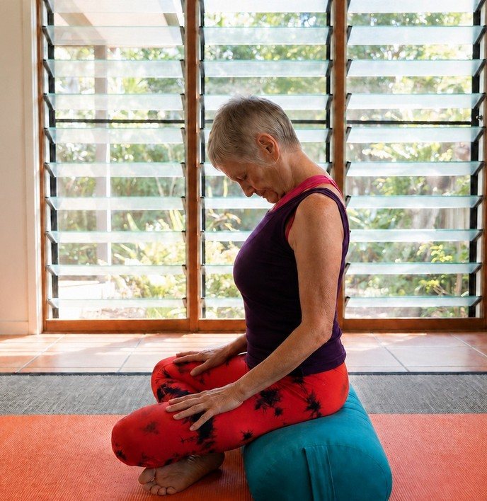 Chris Lalor seated cross-legged on a bolster, eyes lowered, hands resting on the knees, settling into breathing practice