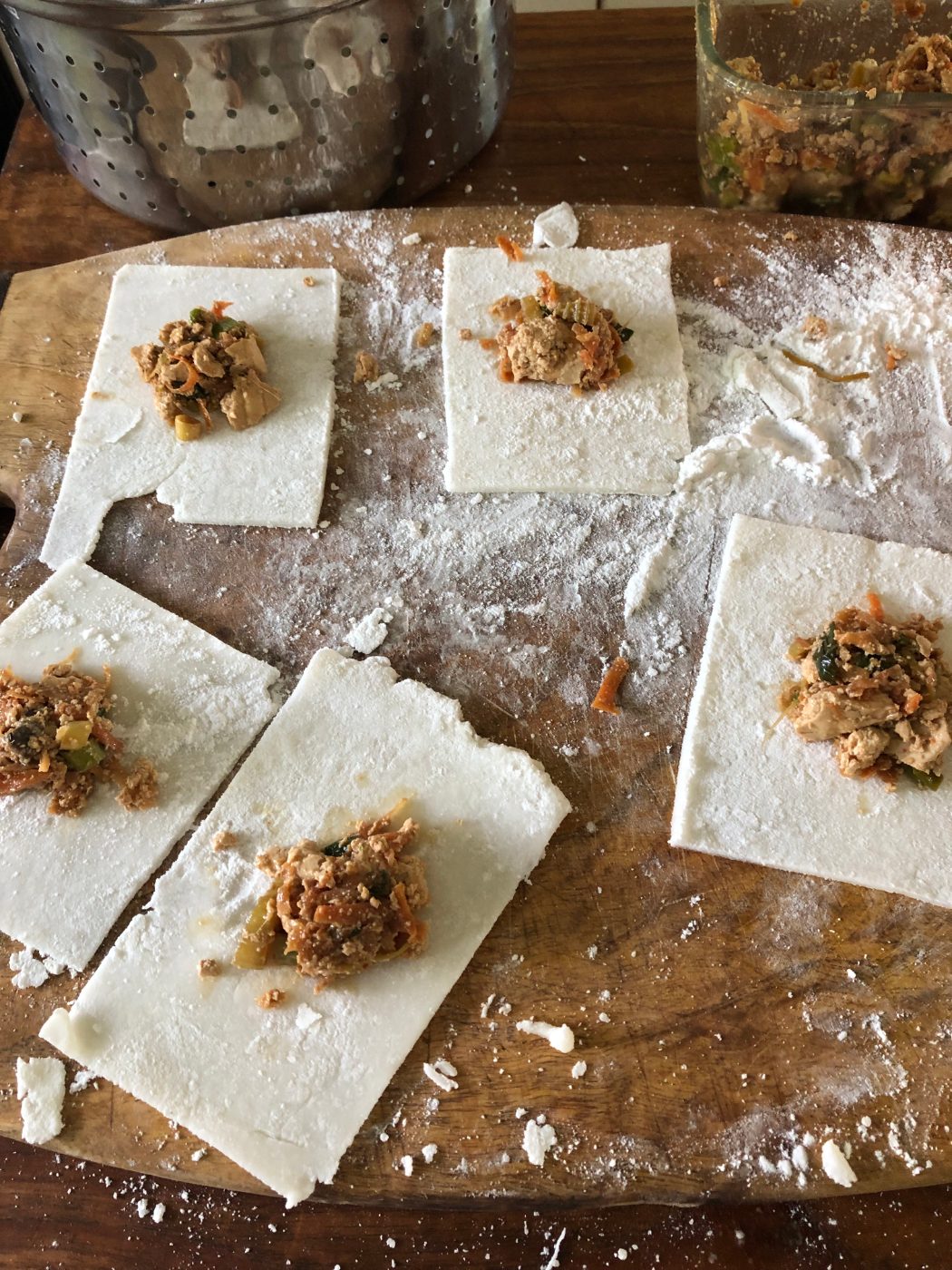 Homemade gluten free wonton wrappers on a floured board, each with a teaspoon of tofu filling
