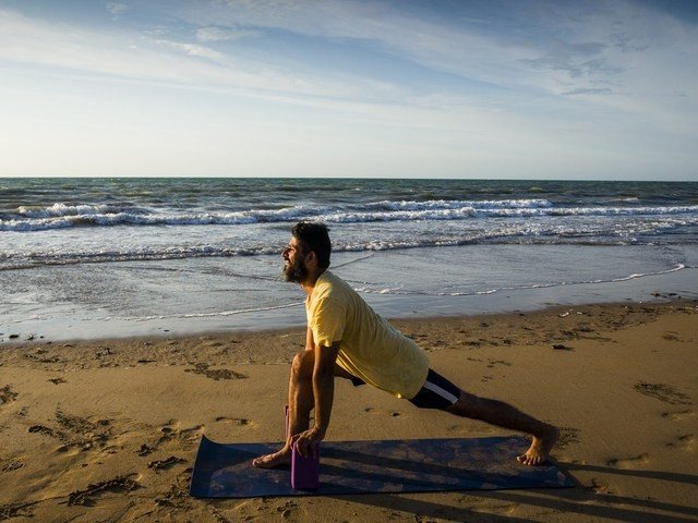 Golfer's back pain: a man in Downward Facing Dog on a beach mat at sunset, weight through the hands and legs
