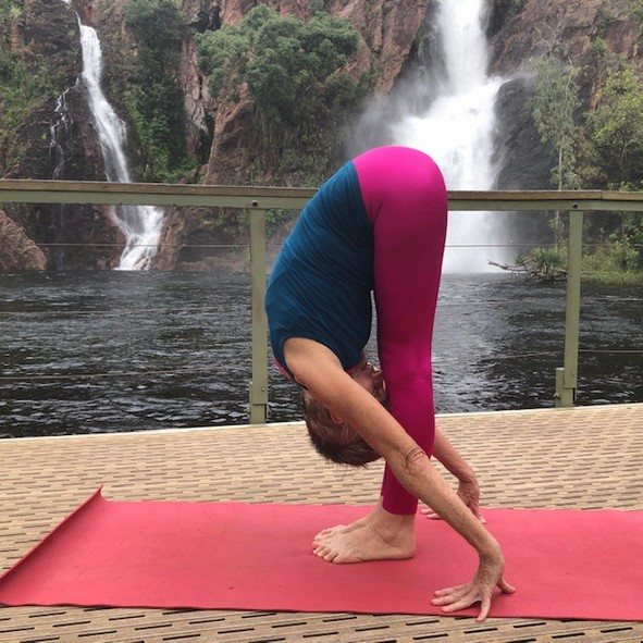 How to get more flexible: Chris Lalor in Standing Forward Bend beside a Top End waterfall, legs straight, fingertips on the mat