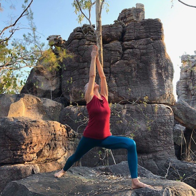 How to improve balance: Chris Lalor in Warrior I on a rock ledge in the Top End, back leg straight, arms reaching up