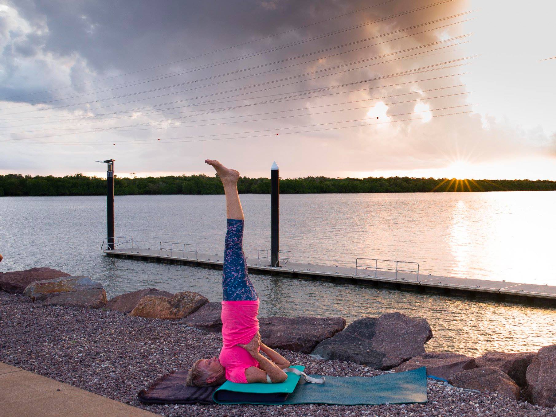 Iyengar yoga shoulderstand (Salamba Sarvangasana) on folded mats with a belt, by the water in Darwin at sunset