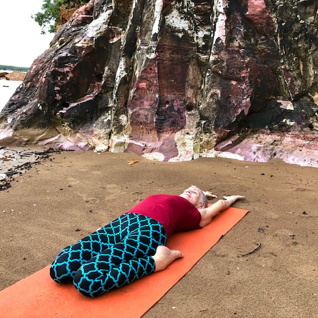 Hip flexor stretch: Reclining Hero Pose on a mat on a Darwin beach below red cliffs
