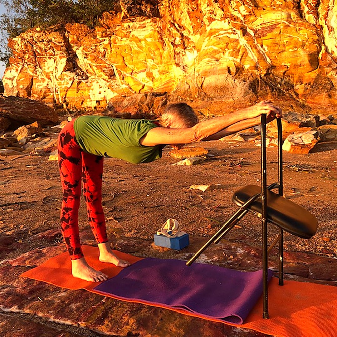 Sitting rising test: Chris Lalor in a half forward bend with her hands on a chair, legs straight, on rocks in the Top End