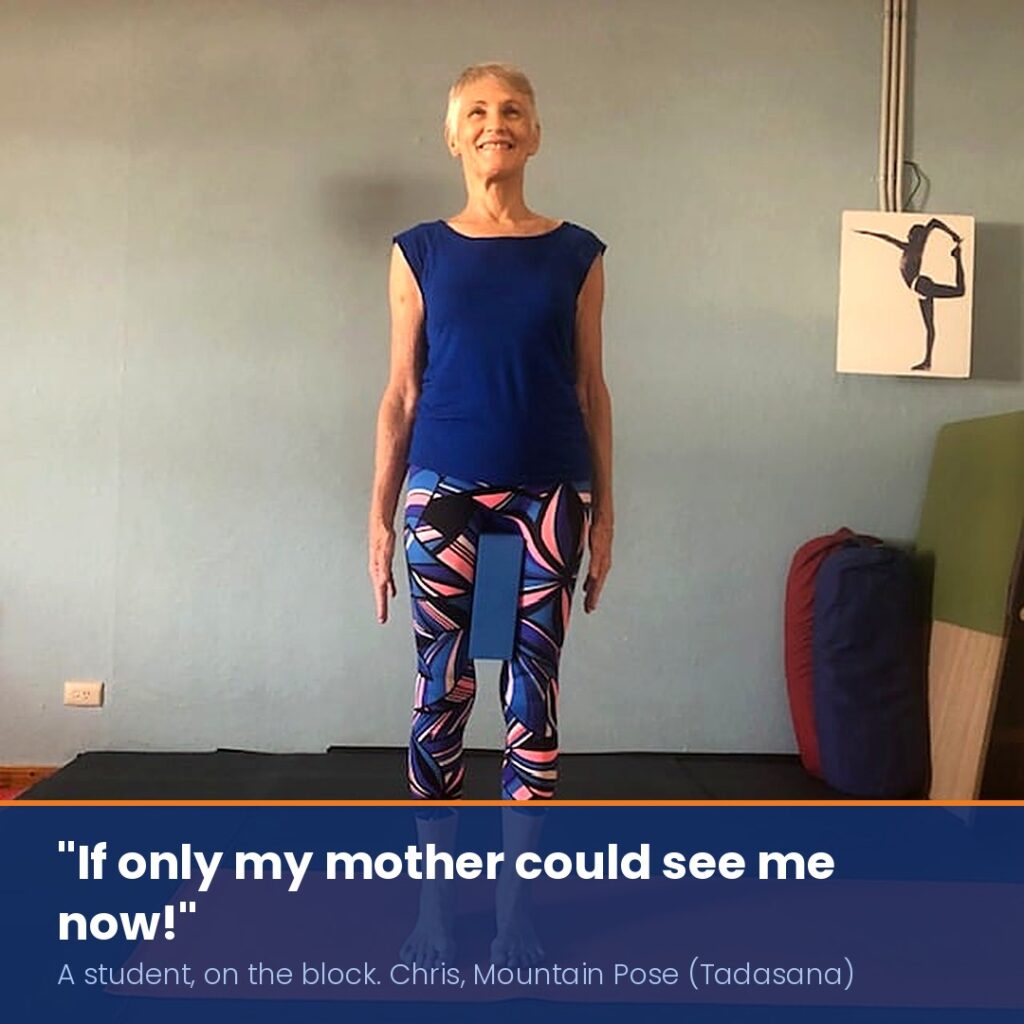Chris Lalor smiling in Mountain Pose (Tadasana) with a yoga block between her thighs, caption: 