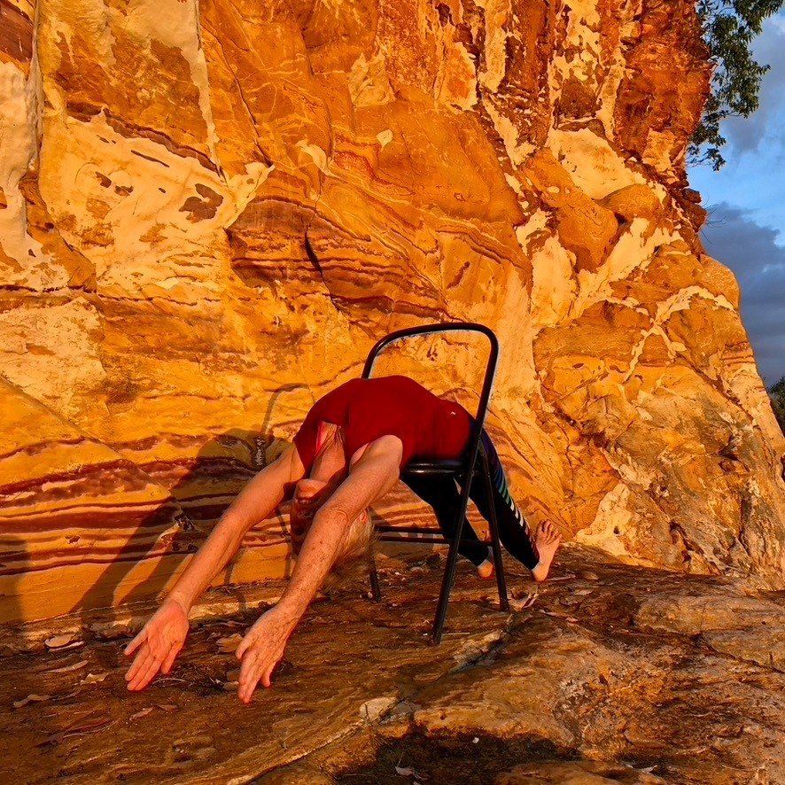 Iyengar yoga Darwin: a supported backbend over a chair on orange rock at sunset in the Top End