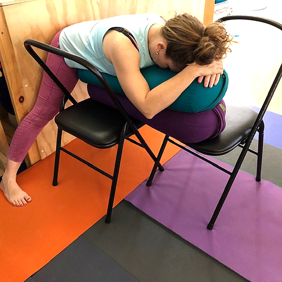 Period pain: Kim resting her head and arms on a bolster across two chairs in a supported wide-legged forward bend