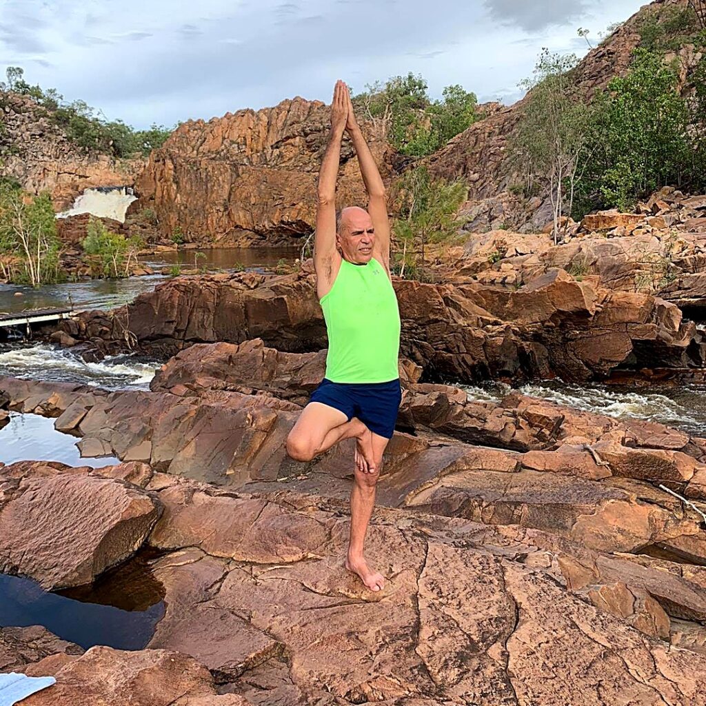 Stuart McGill in Tree Pose with arms raised on rocks at Edith Falls