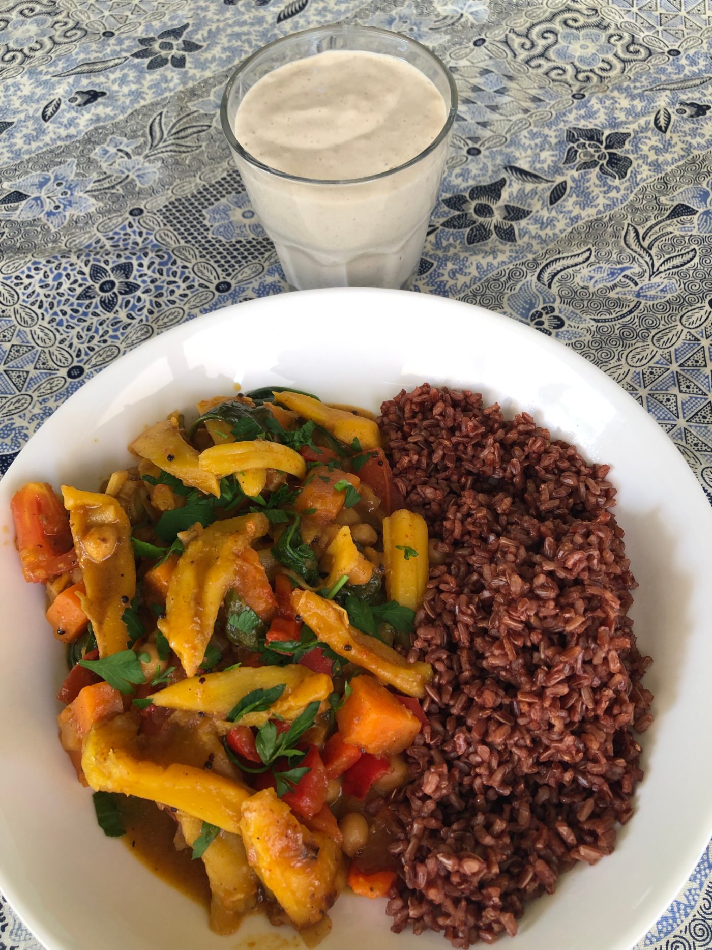 Jackfruit curry with red rice beside a banana smoothie made with silken tofu and soy milk