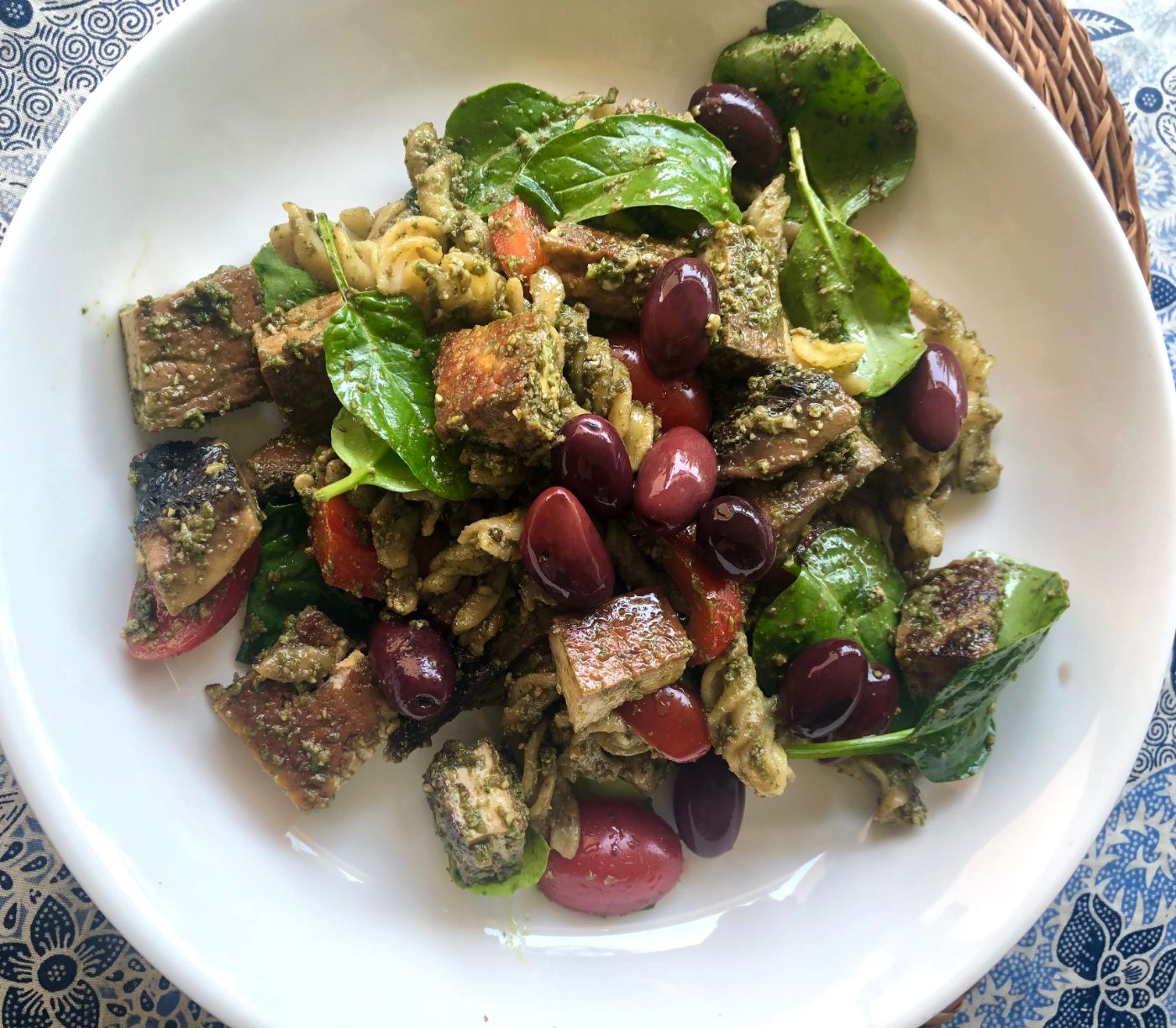 A bowl of lentil pasta with sunflower seed pesto, tofu, mushrooms, olives and baby spinach