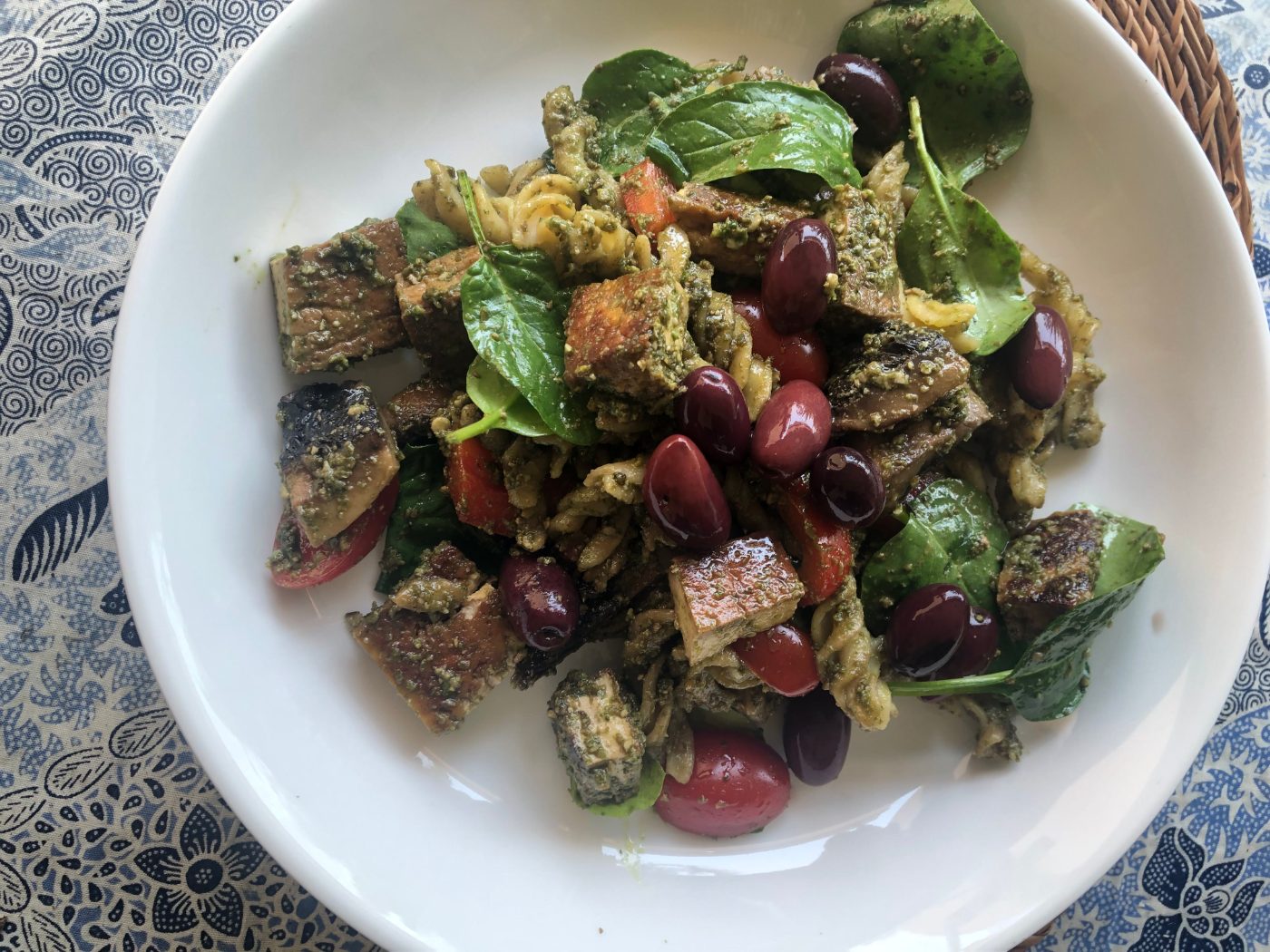Lentil pasta tossed with sunflower seed pesto, olives and baby spinach