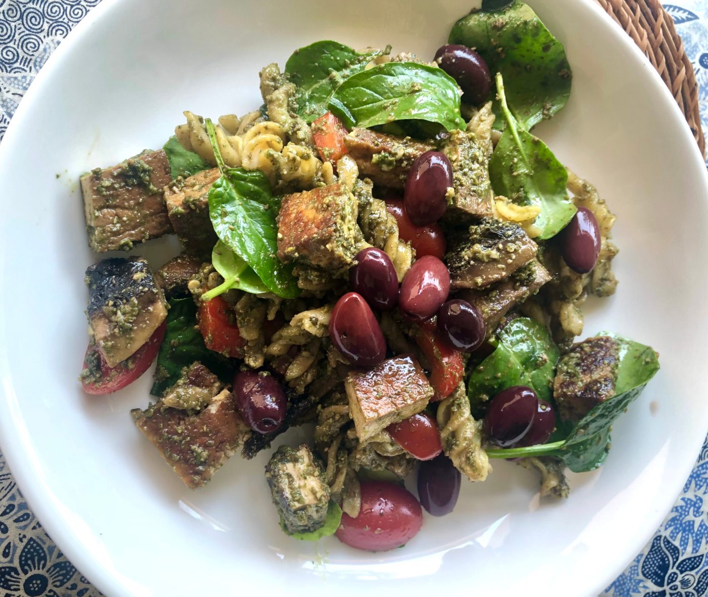 Lentil pasta with baby spinach, baby tomatoes and olives in a white bowl