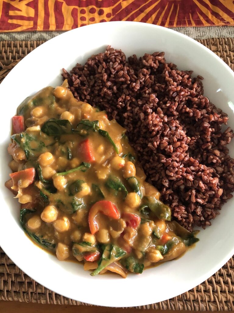 Mango chickpea curry with spinach and red capsicum, served with red rice in a white bowl