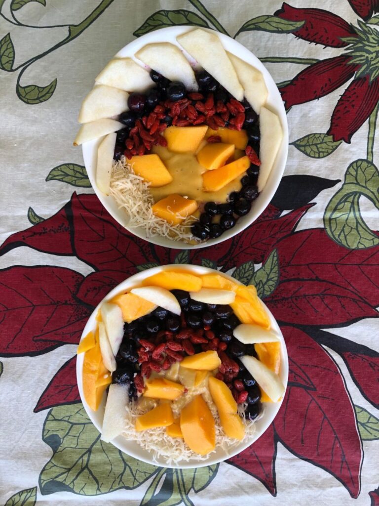 Two mango smoothie bowls topped with mango, pear, blueberries, goji berries and coconut
