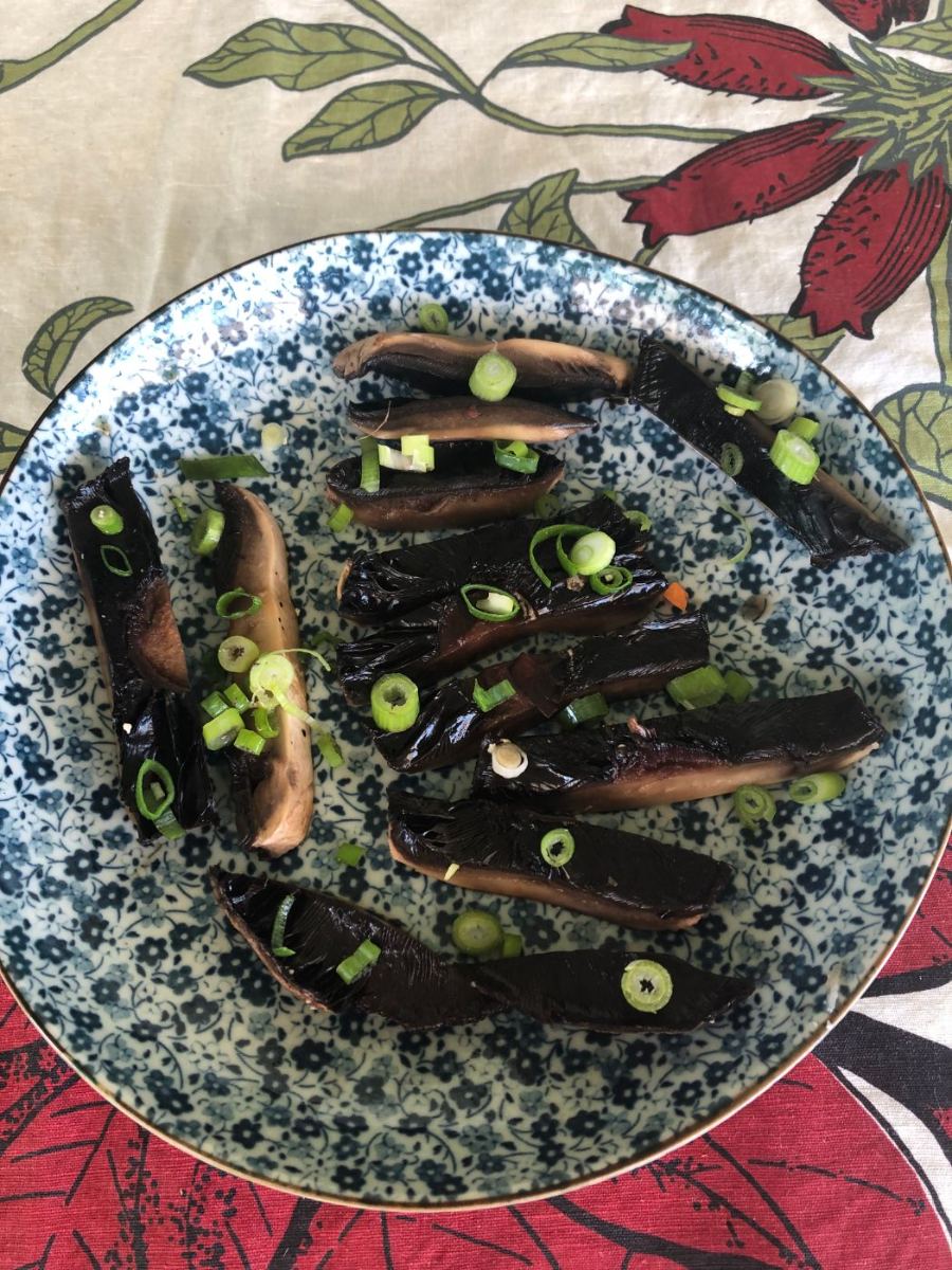 Marinated mushrooms, thinly sliced on a blue and white plate with spring onions