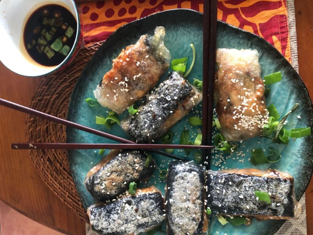 Pan fried tofu rice paper rolls with nori and sesame seeds on a plate, with a bowl of tamari dipping sauce