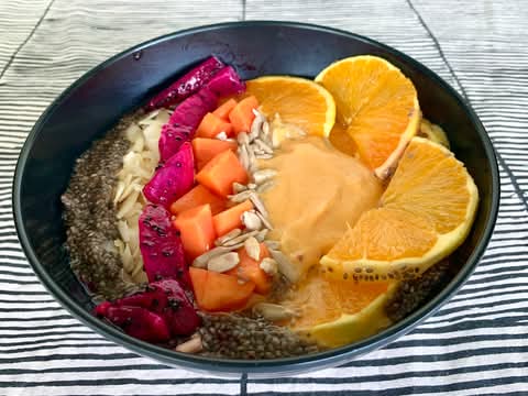 Papaya smoothie bowl topped with dragon fruit, orange slices, papaya, seeds and coconut flakes in a black bowl