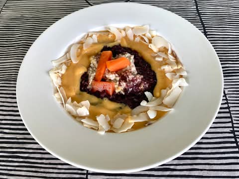 Papaya smoothie over black rice pudding and oats on a white plate, topped with coconut flakes