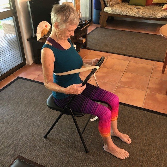 A student sitting backwards on a chair with belts, chest lifted, eyes closed, during a Flametree pranayama class