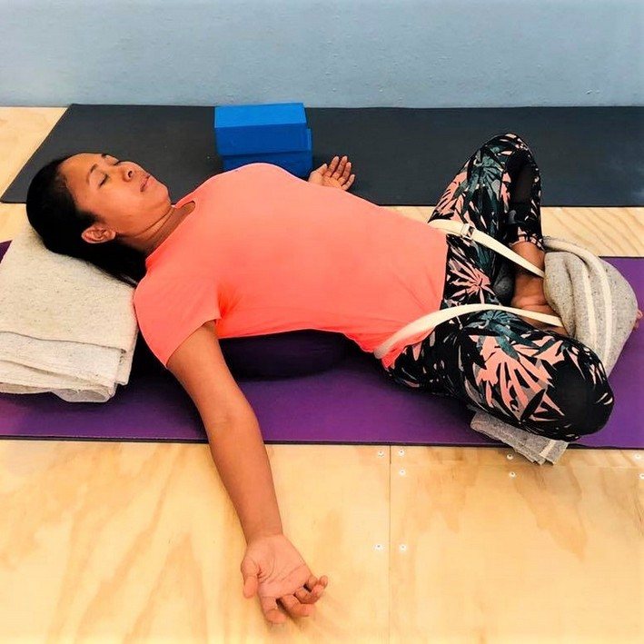 A student resting in a supported restorative yoga pose on a bolster and blankets during a Flametree class