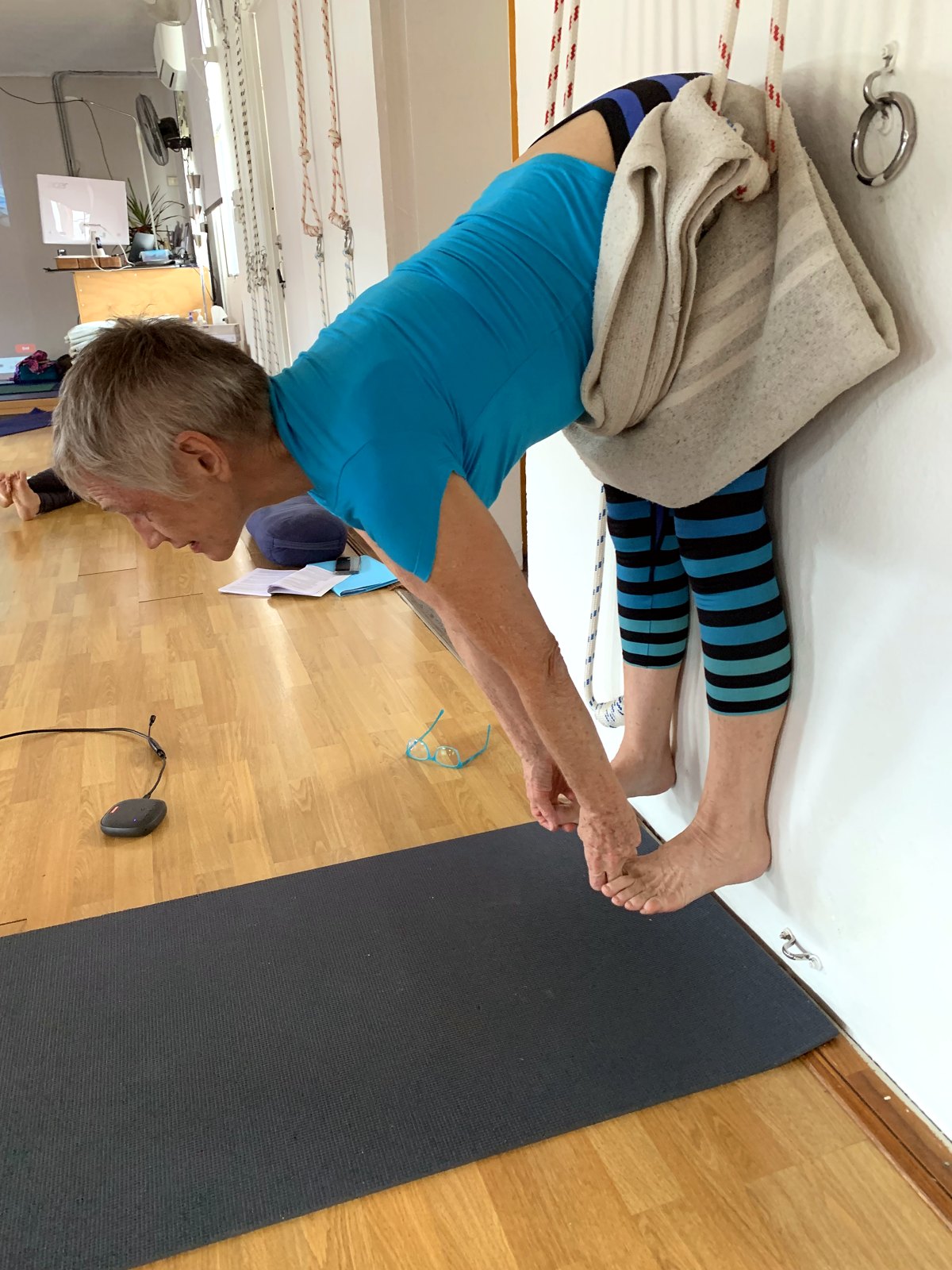 Standing forward bend with a wall rope and blanket at Flametree Yoga Studio